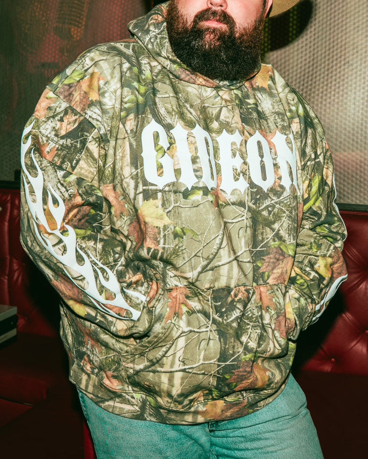 Person wearing a camouflage hoodie with 'GIDEON' printed on it, and flame print sleeves.