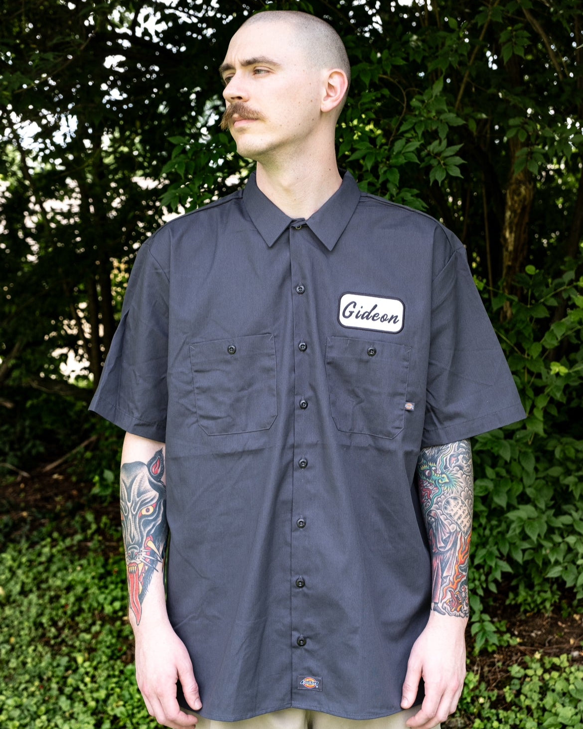 FRONT IMAGE OF WORK SHIRT. EMBROIDERED GIDEON NAME PATCH. PRINT OF GIDEON LLC SPEED SHOP "WE BUILD EM FAST. WE BUILD TO LAST" WHITE PRINT ON CHARCOAL/GREY DICKIES BUTTON UP COLLARED WORK SHIRT.