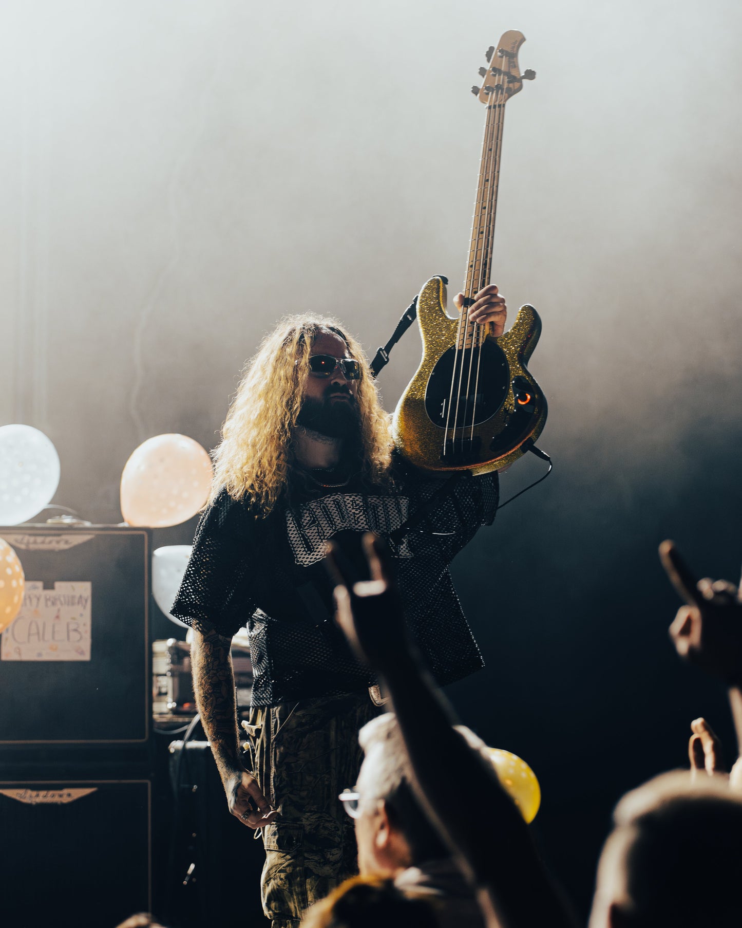 BASSIST FOR GIDEON CALEB DERUSHA HOLDING UP BASS AT A SHOW IN EUROPE. WEARING GIDEON SCRIMMAGE JERSEY