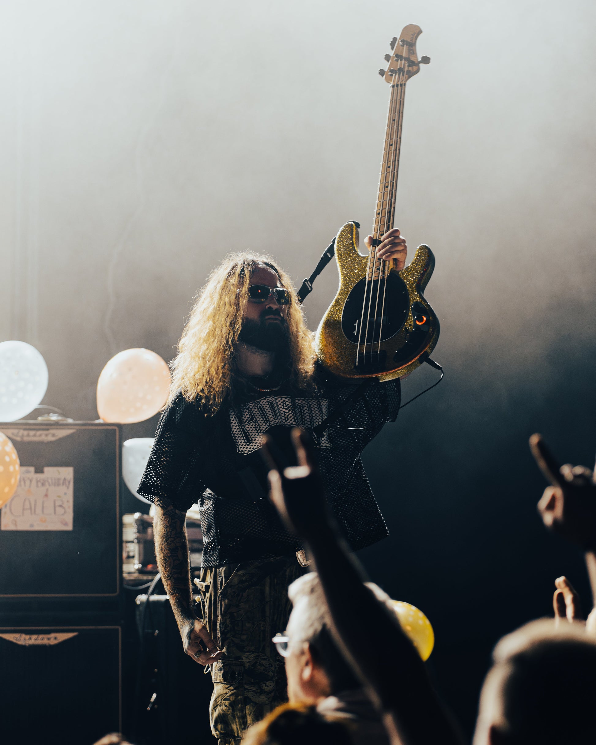 BASSIST FOR GIDEON CALEB DERUSHA HOLDING UP BASS AT A SHOW IN EUROPE. WEARING GIDEON SCRIMMAGE JERSEY