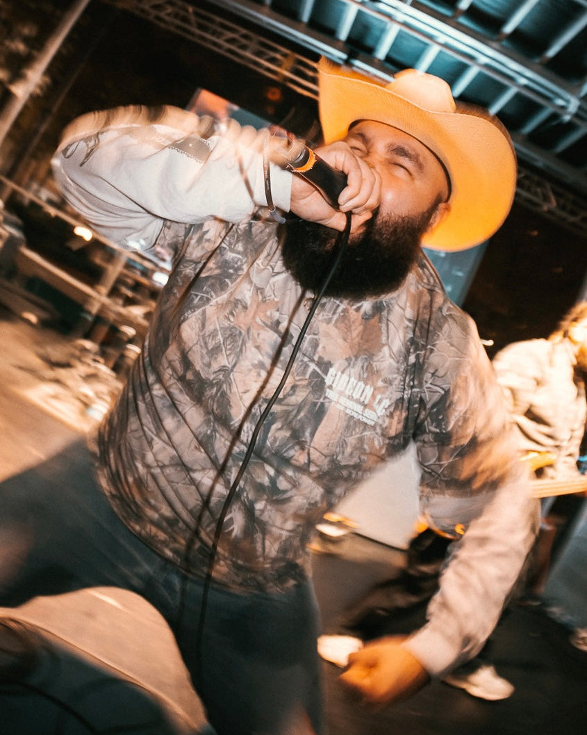 DANIEL MCWHORTER THE VOCALIST OF GIDEON LIVE ON STAGE WEARING CAMO LONG-SLEEVE WITH WHITE SLEEVES WITH CHAINSAWS