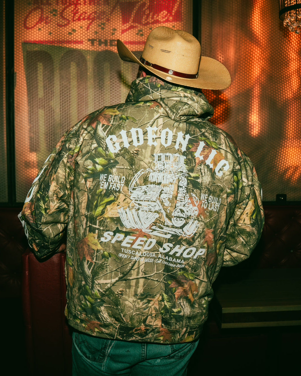 Person wearing a camouflage jacket with text Gideon Speed Shop