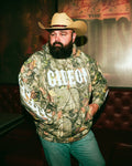 Daniel McWhorter wearing a camouflage hoodie with 'Gideon' text and flame print sleeves.